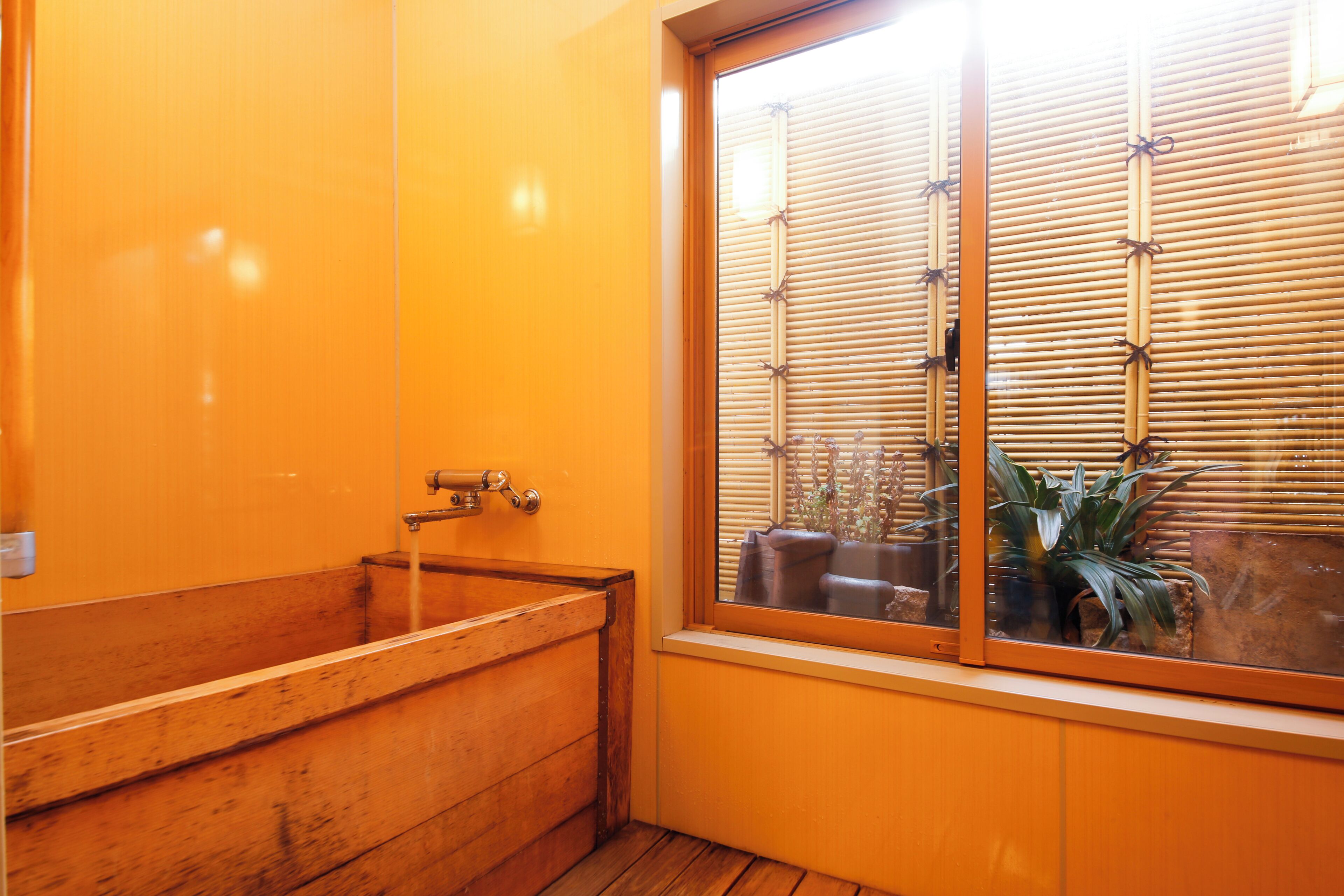 A wooden bathtub in a room with orange walls and a window with bamboo blinds.