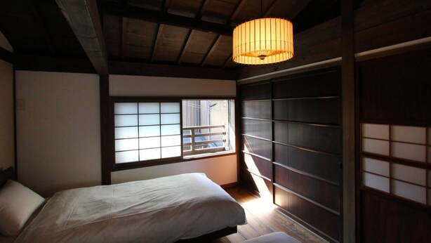 A traditional Japanese-style bedroom with tatami flooring, a low wooden bed, a shoji screen window, and a hanging paper lantern. - Azuki-an Machiya Holiday House (Kyoto)