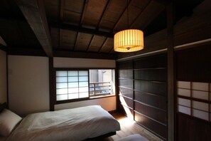 Quarto tradicional japonês, com tatame, cama de madeira baixa, janela com tela shoji e um lampião de papel pendurado.