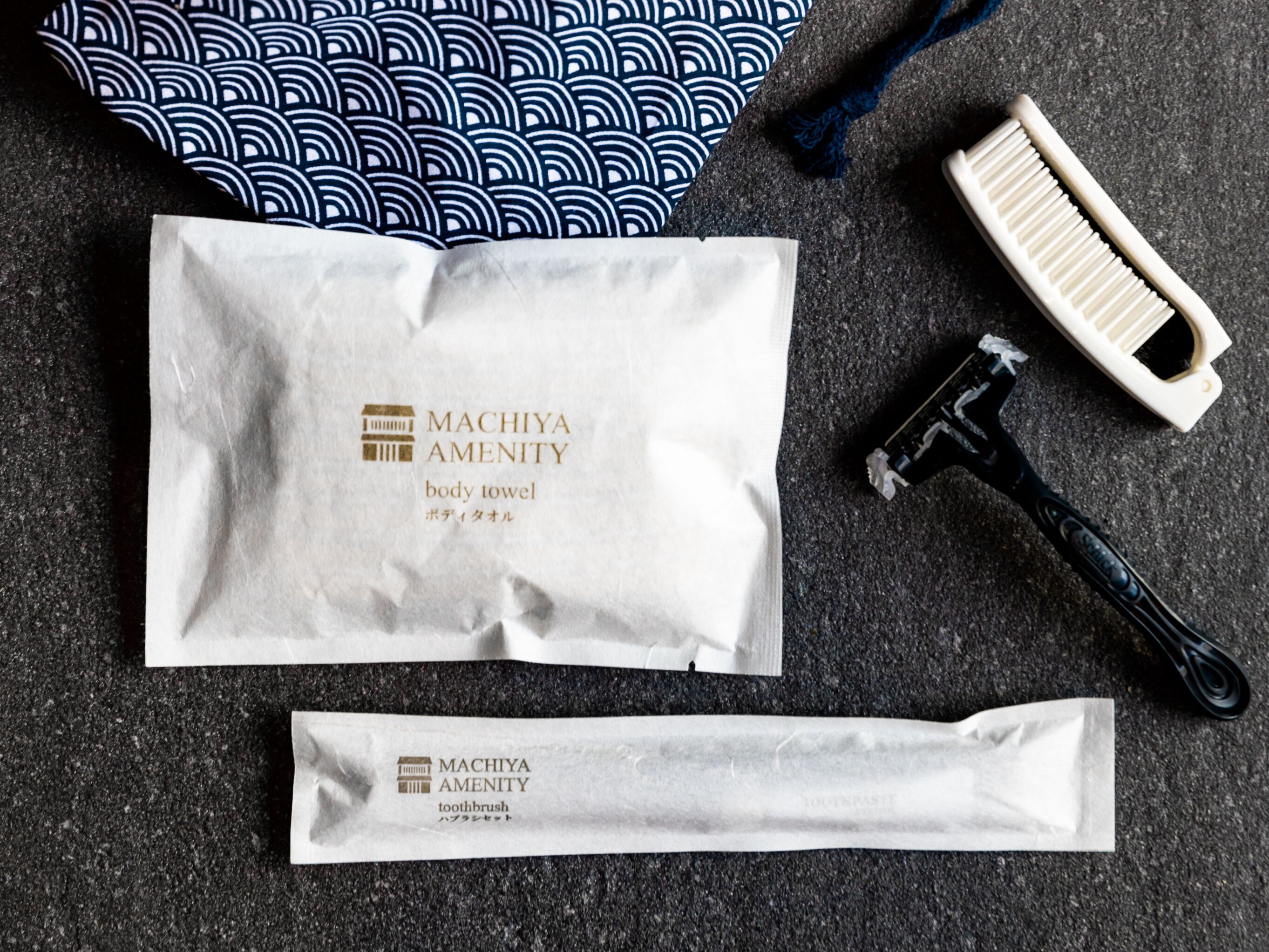 A body towel, toothbrush, and razor from MACHIYA AMENITY on a textured surface.
