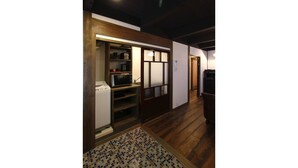 A hallway with wooden flooring, a tiled area rug, and a kitchen area with appliances and cabinets. - Azuki-an Machiya Holiday House (Kyoto)