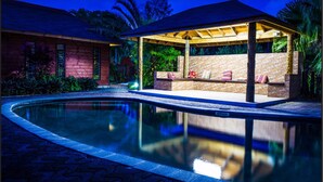 A poolside area with a covered seating area, a brick wall, and a wooden pergola. - Eden's Edge Hotel (Apia)