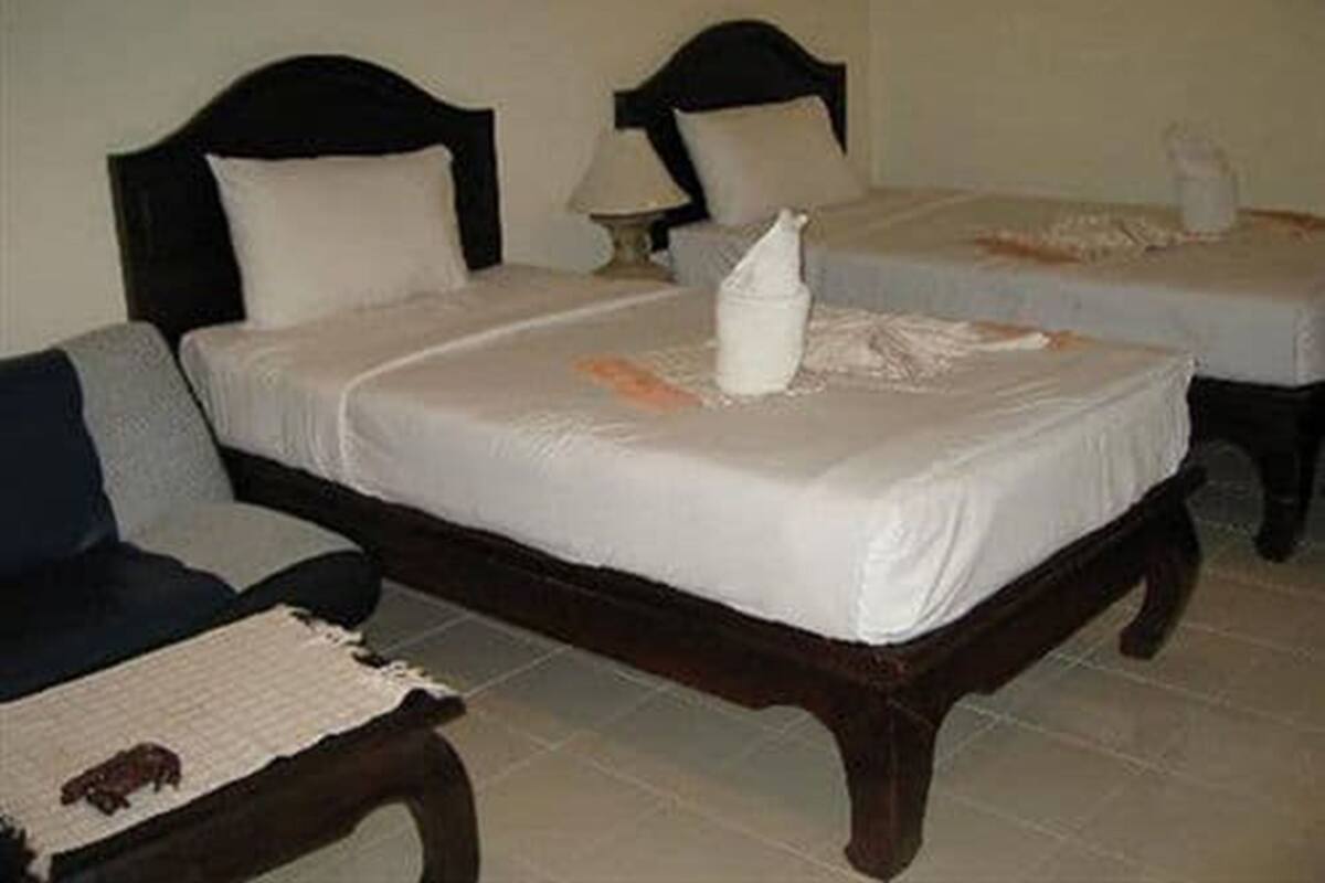 Une chambre d’hôtel avec deux lits simples, une tête de lit en bois, une petite table avec une lampe et une chaise.