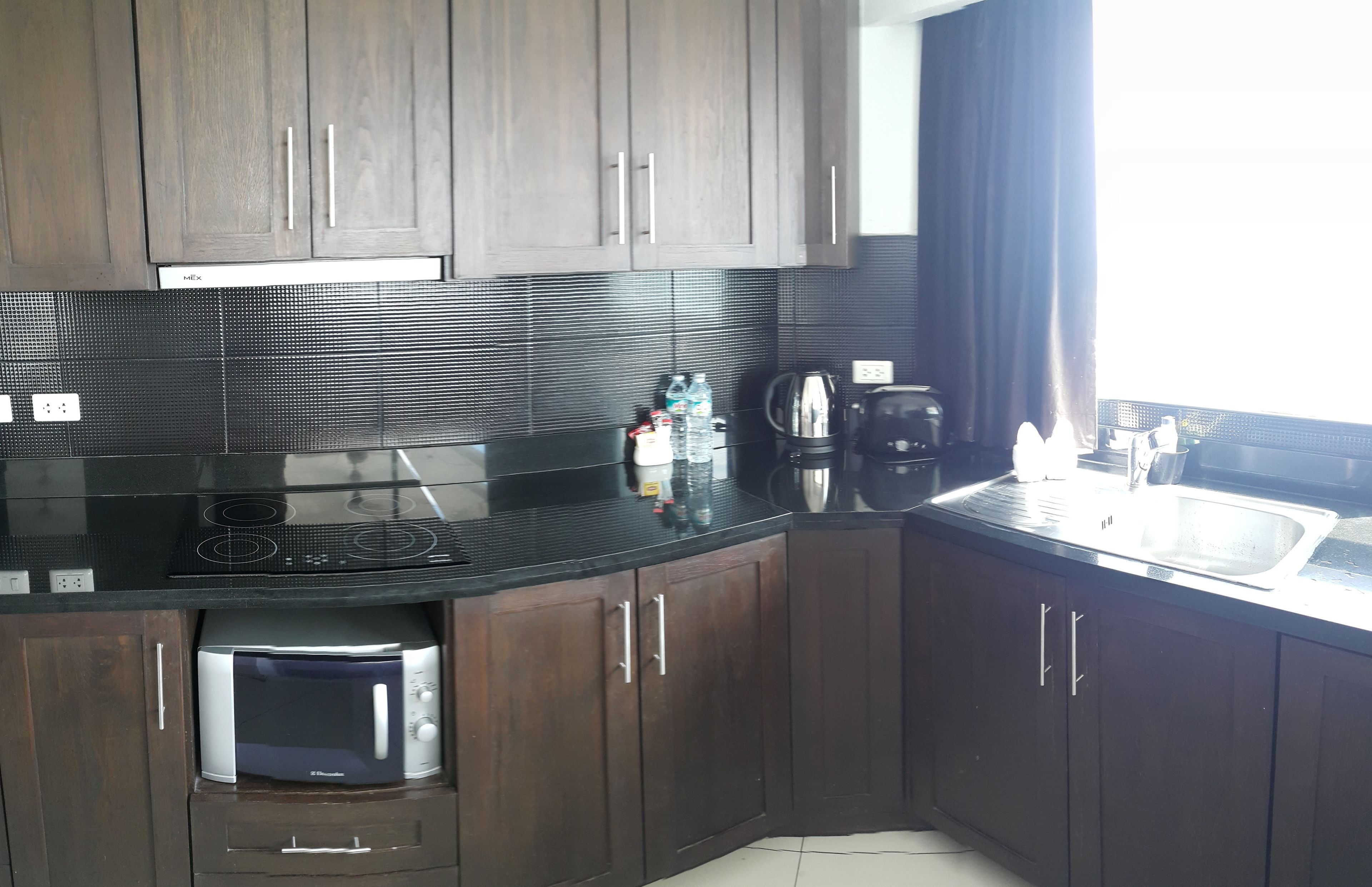A modern kitchen with dark wooden cabinets, a black countertop, a built-in microwave, and a coffee maker.