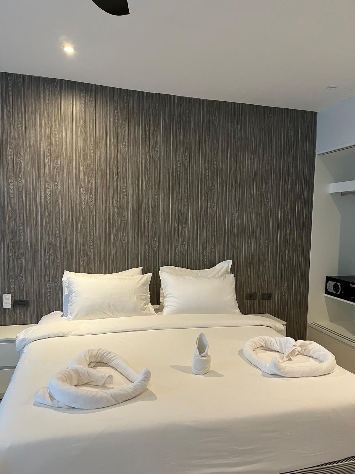A modern hotel room with a large bed, two pillows, a headboard, and a bedside table with a radio.