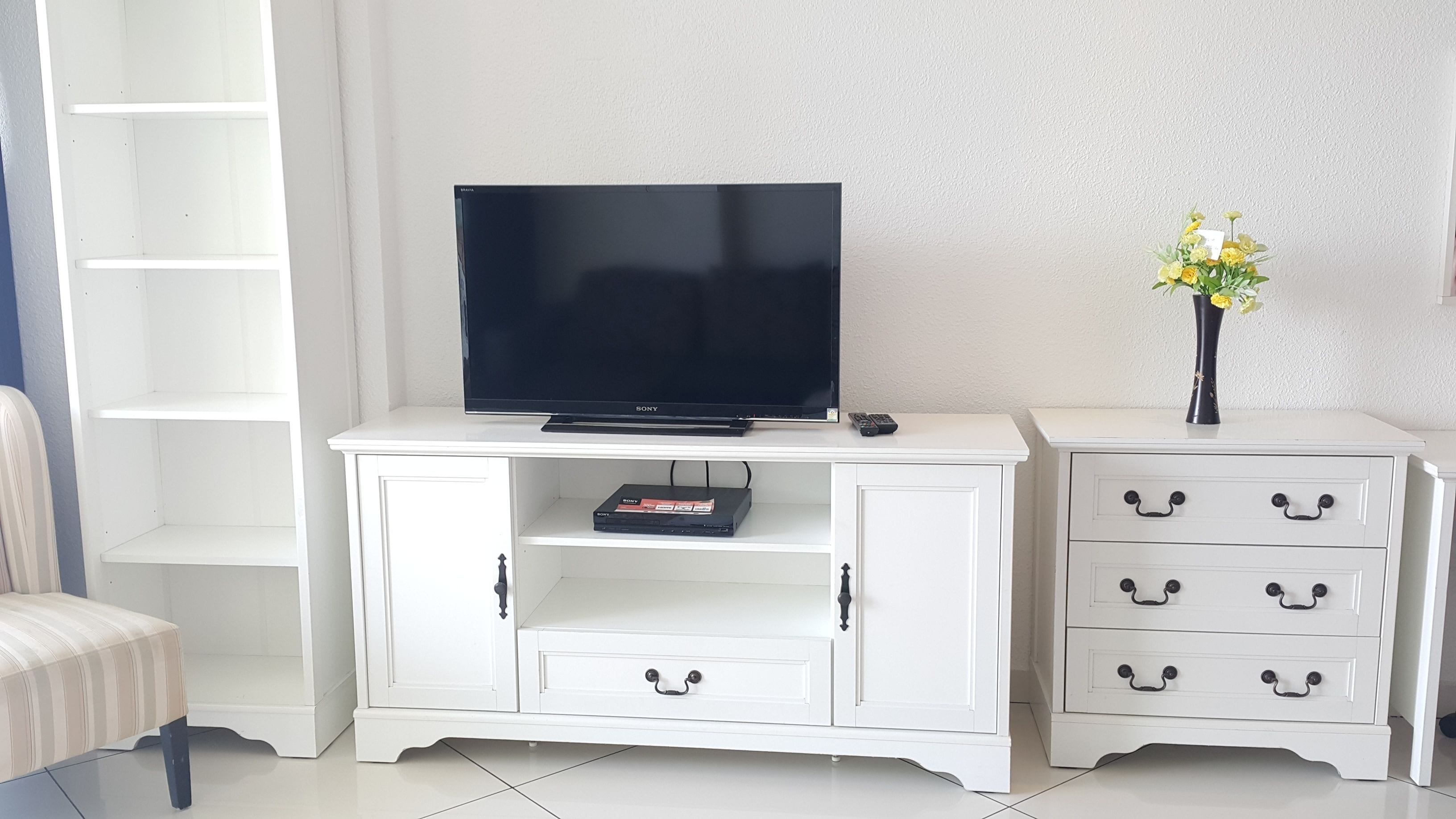 Un mueble blanco de entretenimiento con un televisor de pantalla plana, un reproductor de DVD y un jarrón con flores.