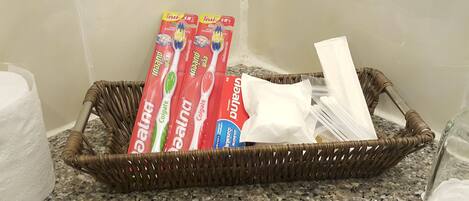 A wicker basket on a granite countertop containing dental hygiene products, including toothpaste and toothbrushes.