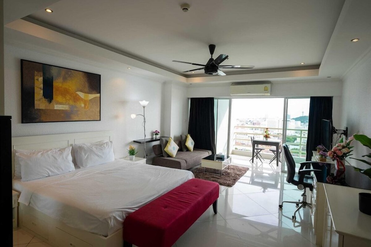 A hotel room with a large bed, a desk, a chair, a sofa, and a view of the city.