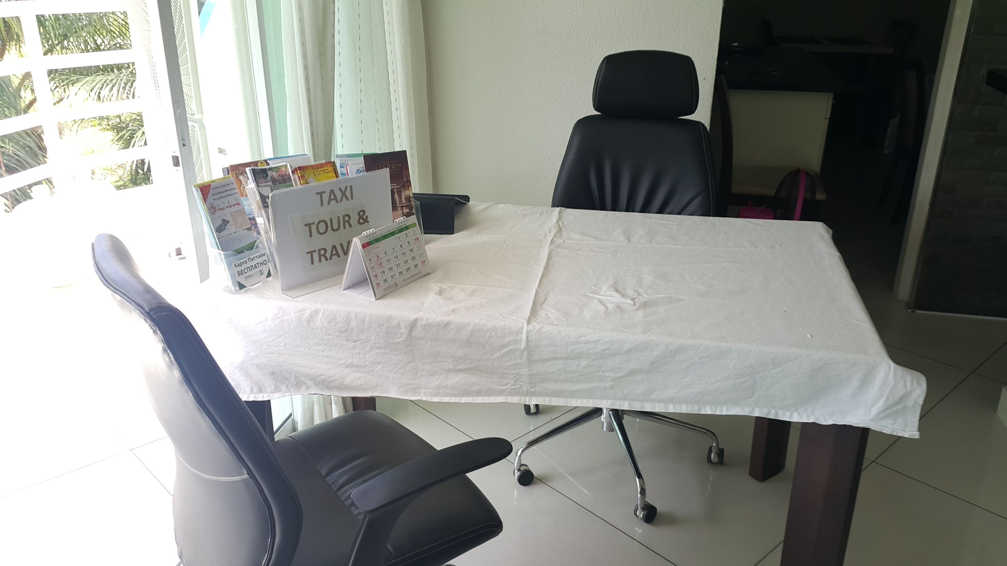 A conference room with a white table, two black office chairs, a calendar, and a sign that reads "TAXI TOUR & TRAVEL".