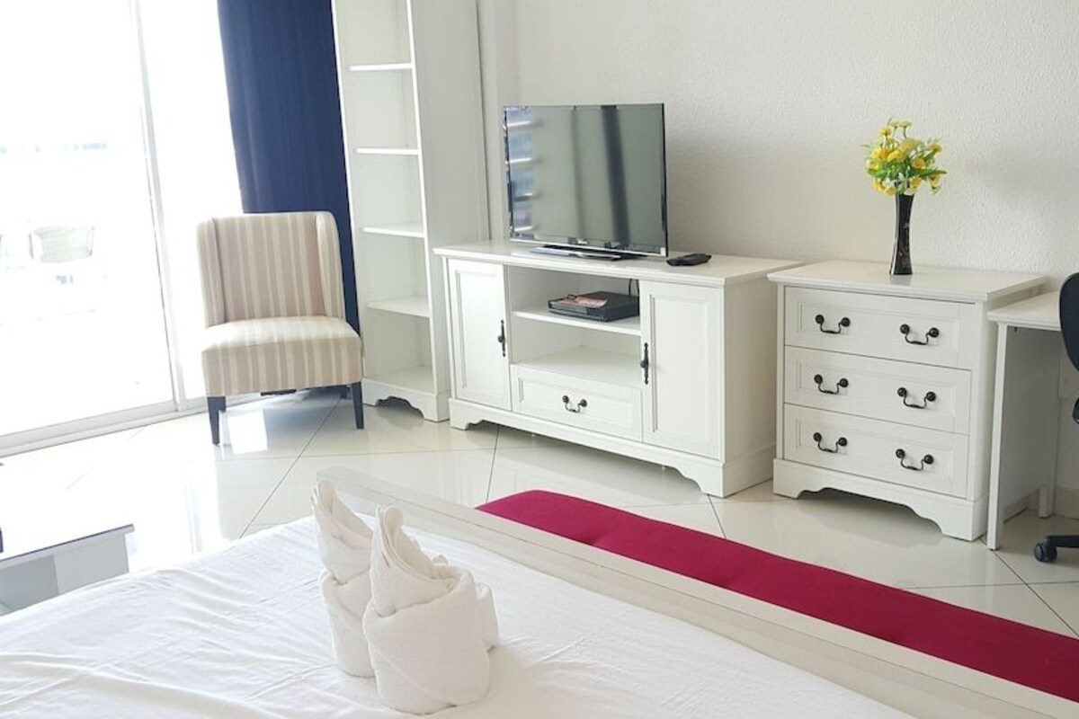 A hotel room with a bed, a TV, a desk, a chair, and a vase with flowers.