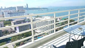 A balcony with a glass table and chairs, overlooking a cityscape with buildings and a marina. - Vtsix Condo Service at View Talay Condo (Pattaya)
