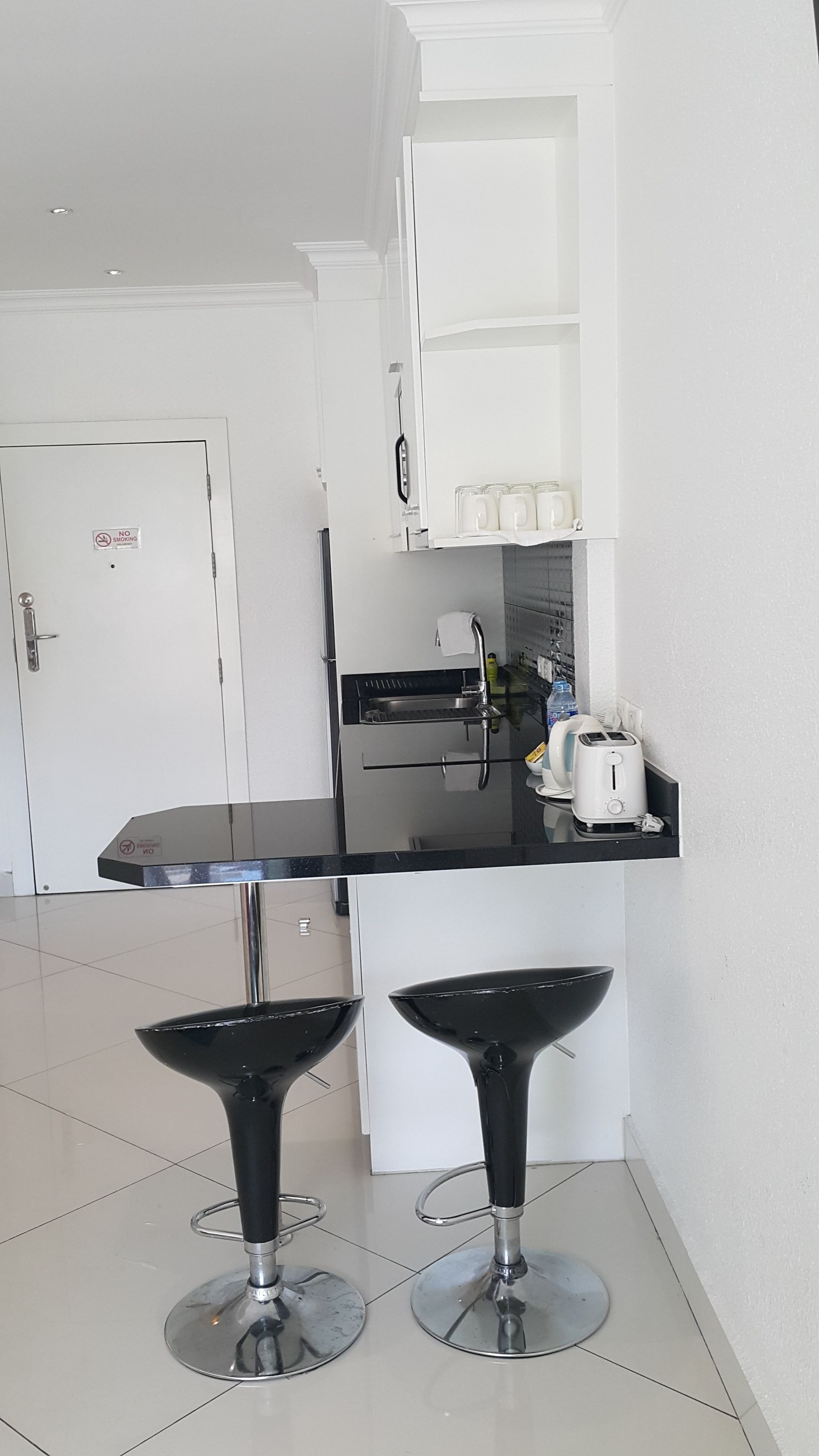 Eine moderne Küche mit einem schwarzen Barhocker, einem weißen Schrank und einem Rauchverbot-Schild an der Tür.