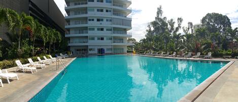 A swimming pool with lounge chairs and a multi-story building in the background.