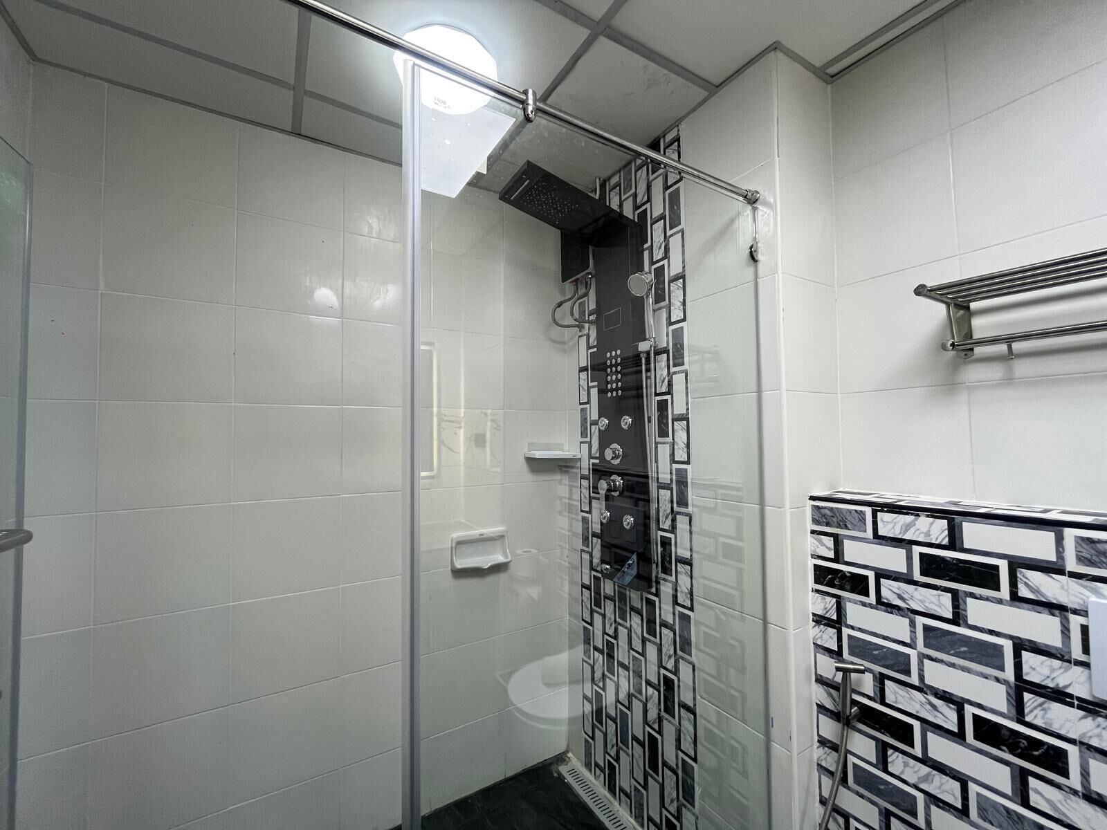 A bathroom with white tiles, a glass shower enclosure, a black and white patterned wall, and a towel rack.