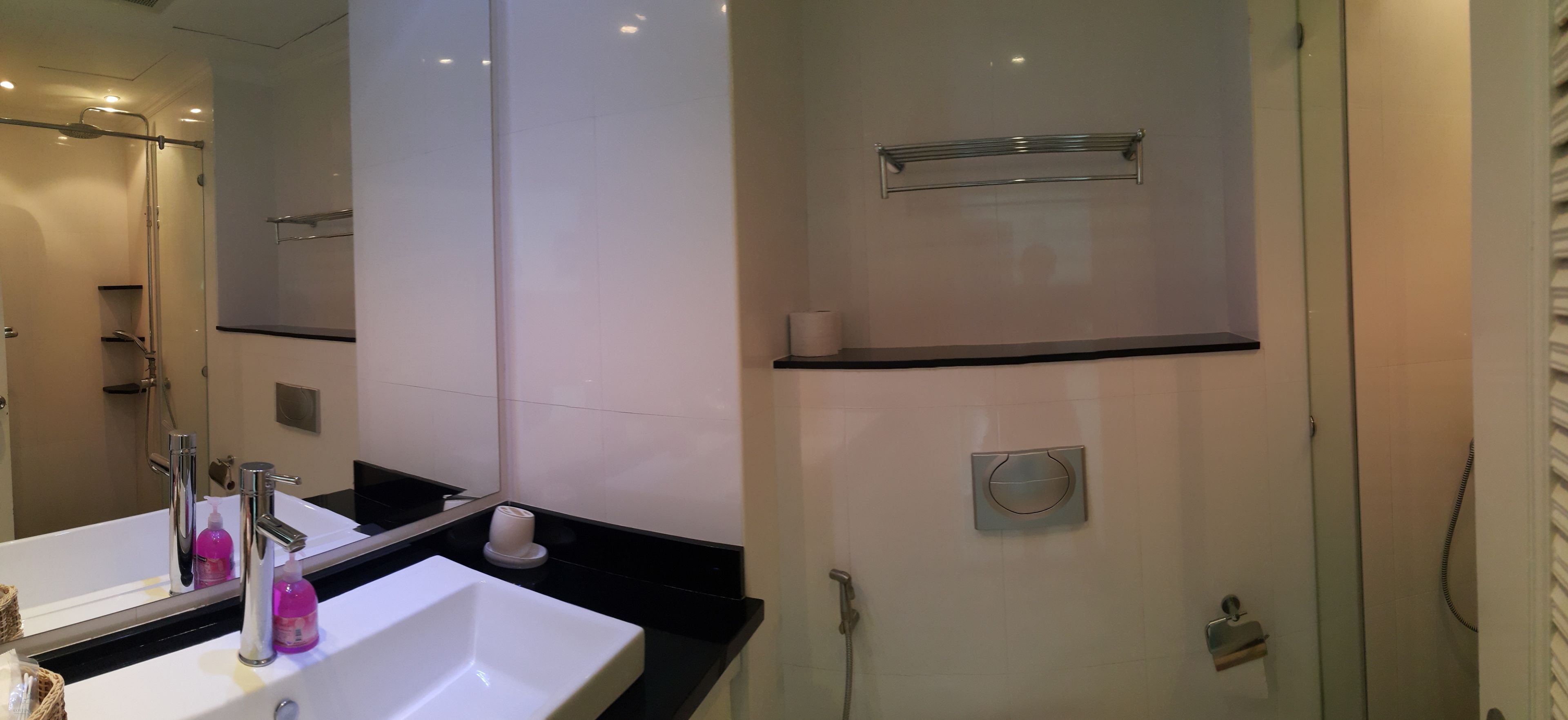 A modern bathroom with a white sink, a large mirror, a shower area, and a towel rack.