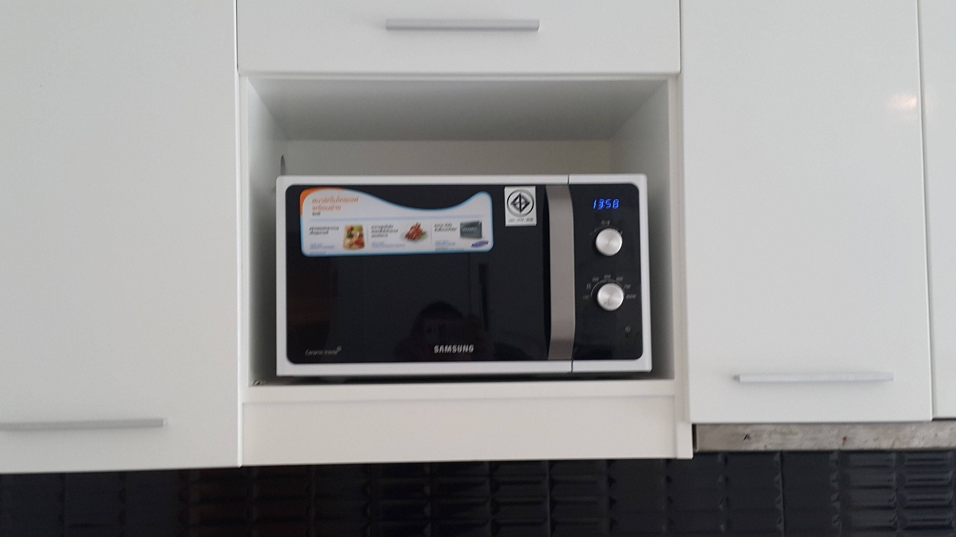 A microwave in a white cabinet with a digital display and control buttons.