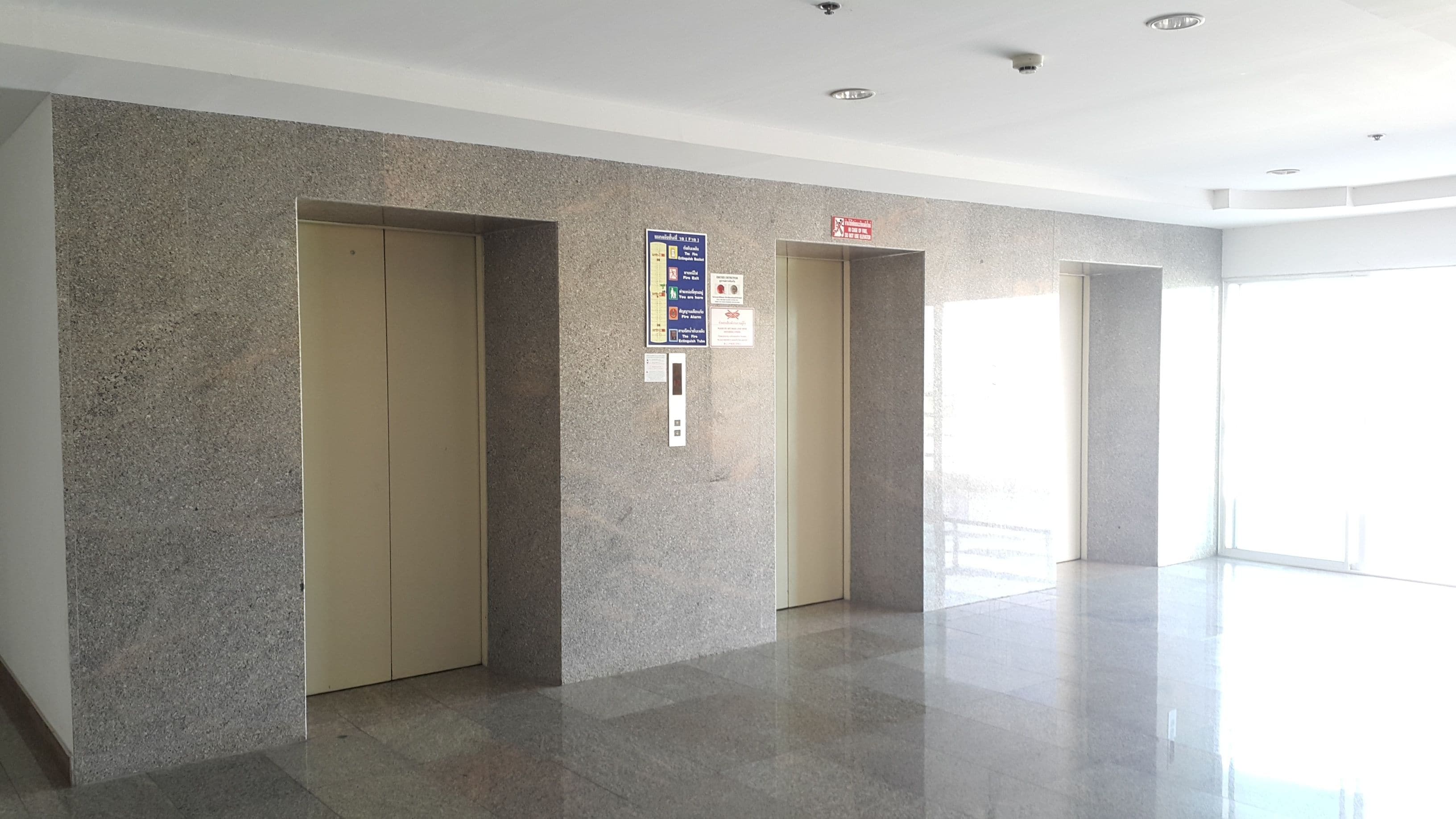 A modern elevator area with granite walls and a polished floor, featuring a sign with emergency instructions.