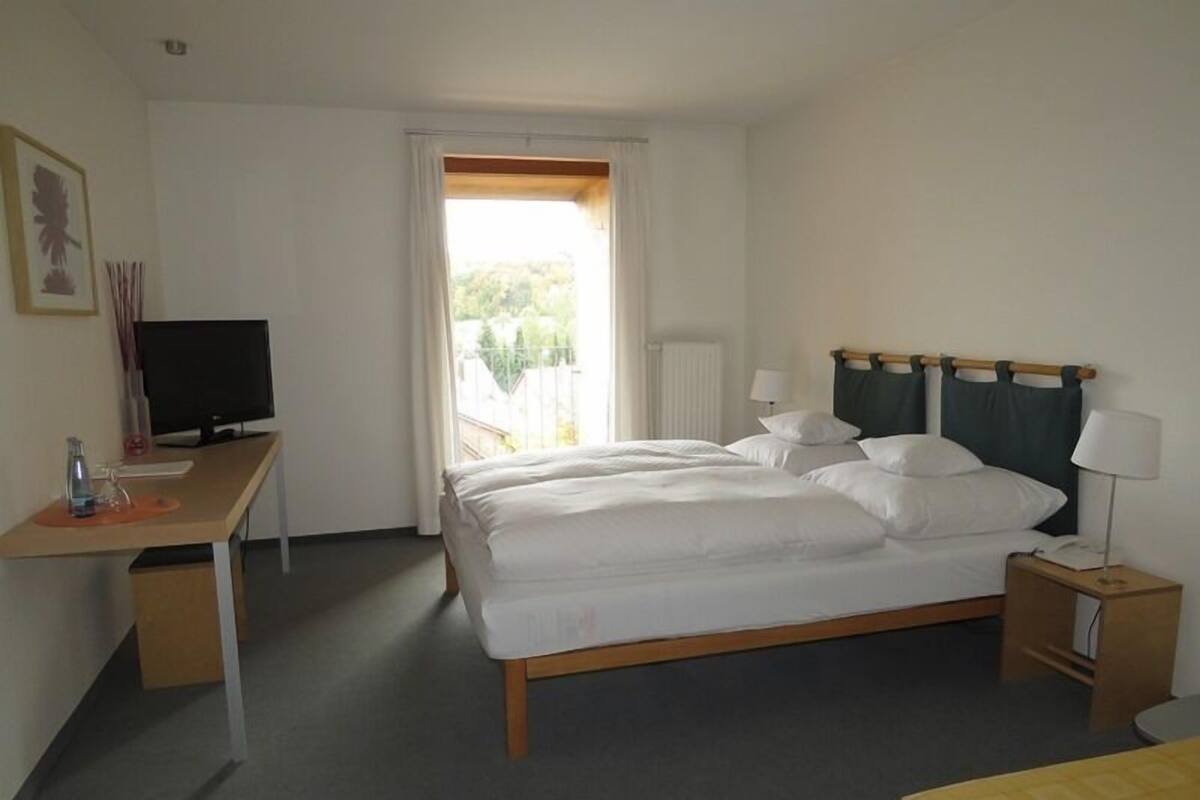 A hotel room with a bed, a desk, a television, and a window with curtains.