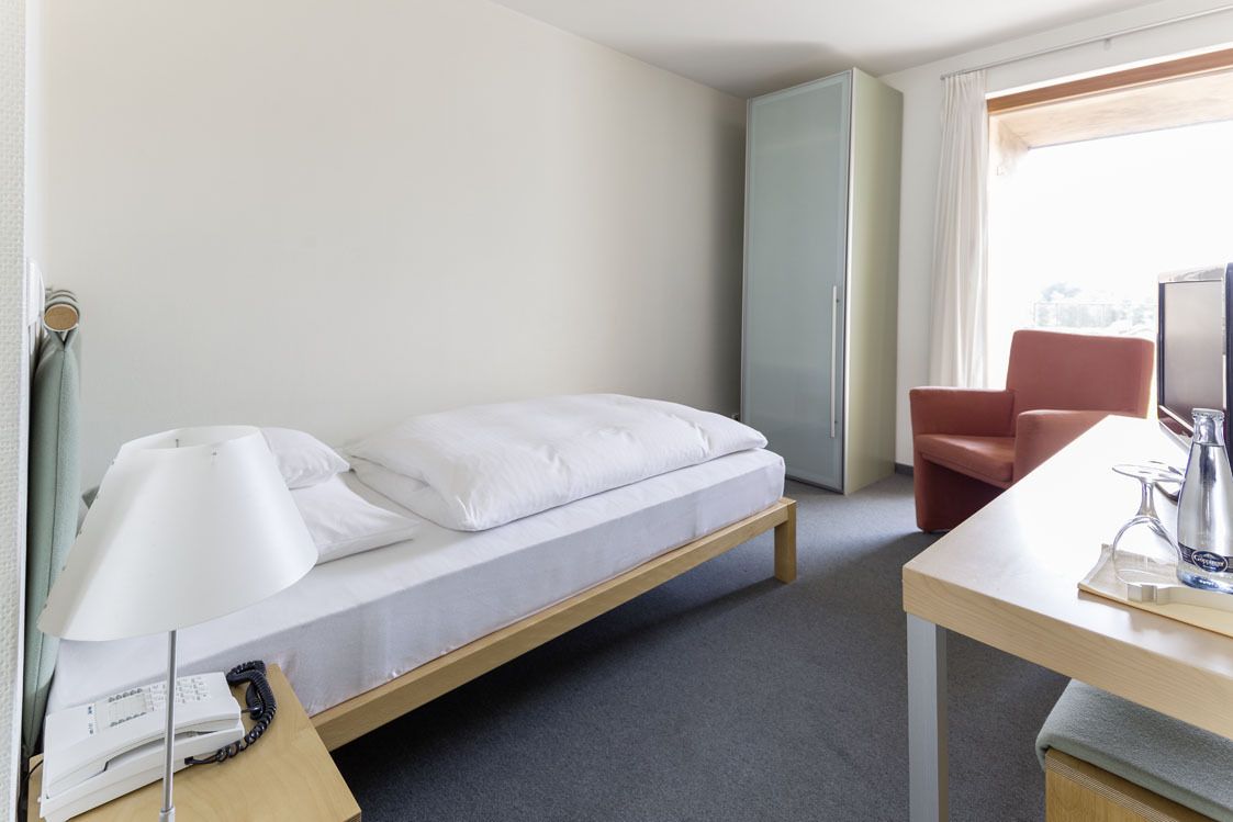Een hotelkamer met een enkel bed, een bureau met lamp, een stoel en een televisie.