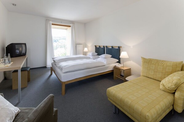 Una habitación de hotel con cama, mesitas de noche, televisor y escritorio con silla.