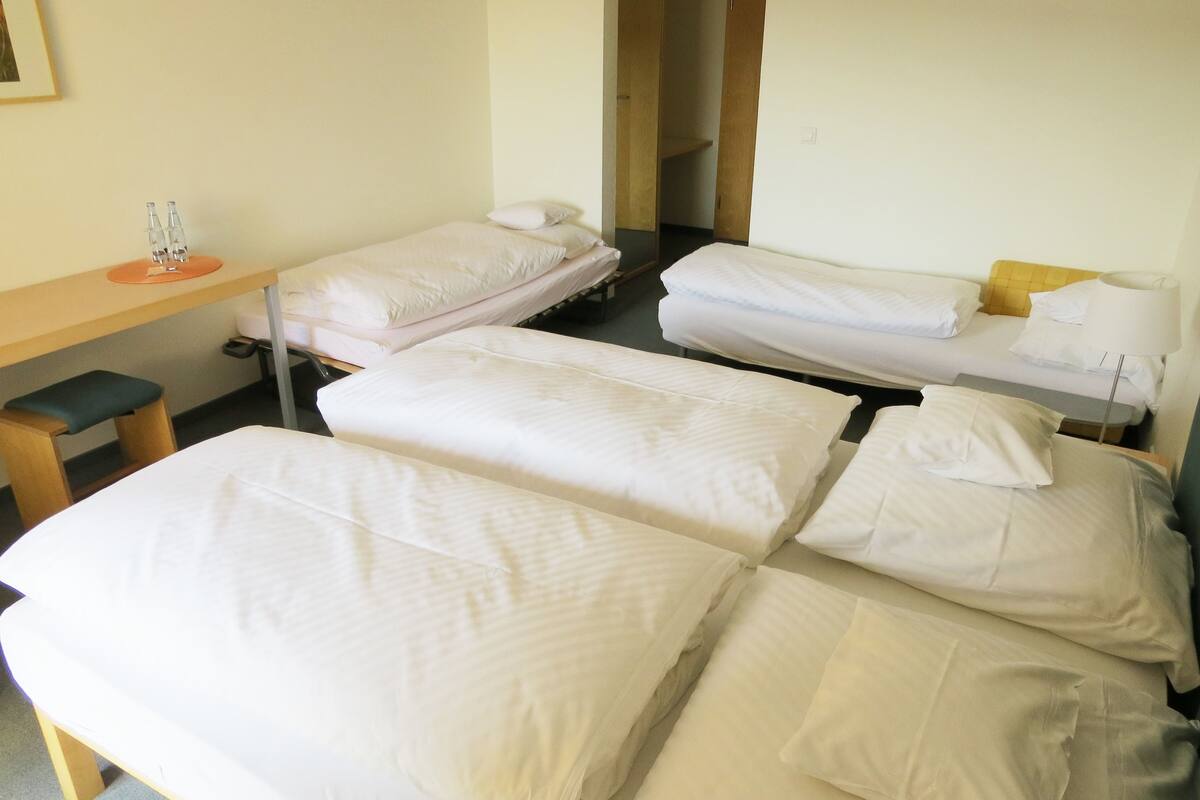 A hotel room with three single beds, a desk, and a chair.