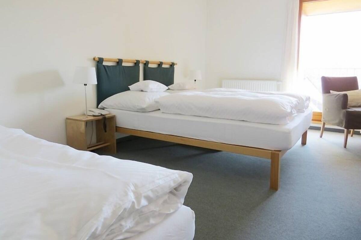 A hotel room with two beds, a nightstand with a lamp, a chair, and a window with curtains.