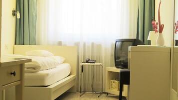 Una habitación de hotel con cama, escritorio con televisor, un mueble pequeño y un radiador.