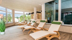 A sunlit room with wooden lounge chairs and large windows offering a view of the outdoors. - Wellnesshotel Sonnenhof & Sonnhalde (Uehlingen-Birkendorf)
