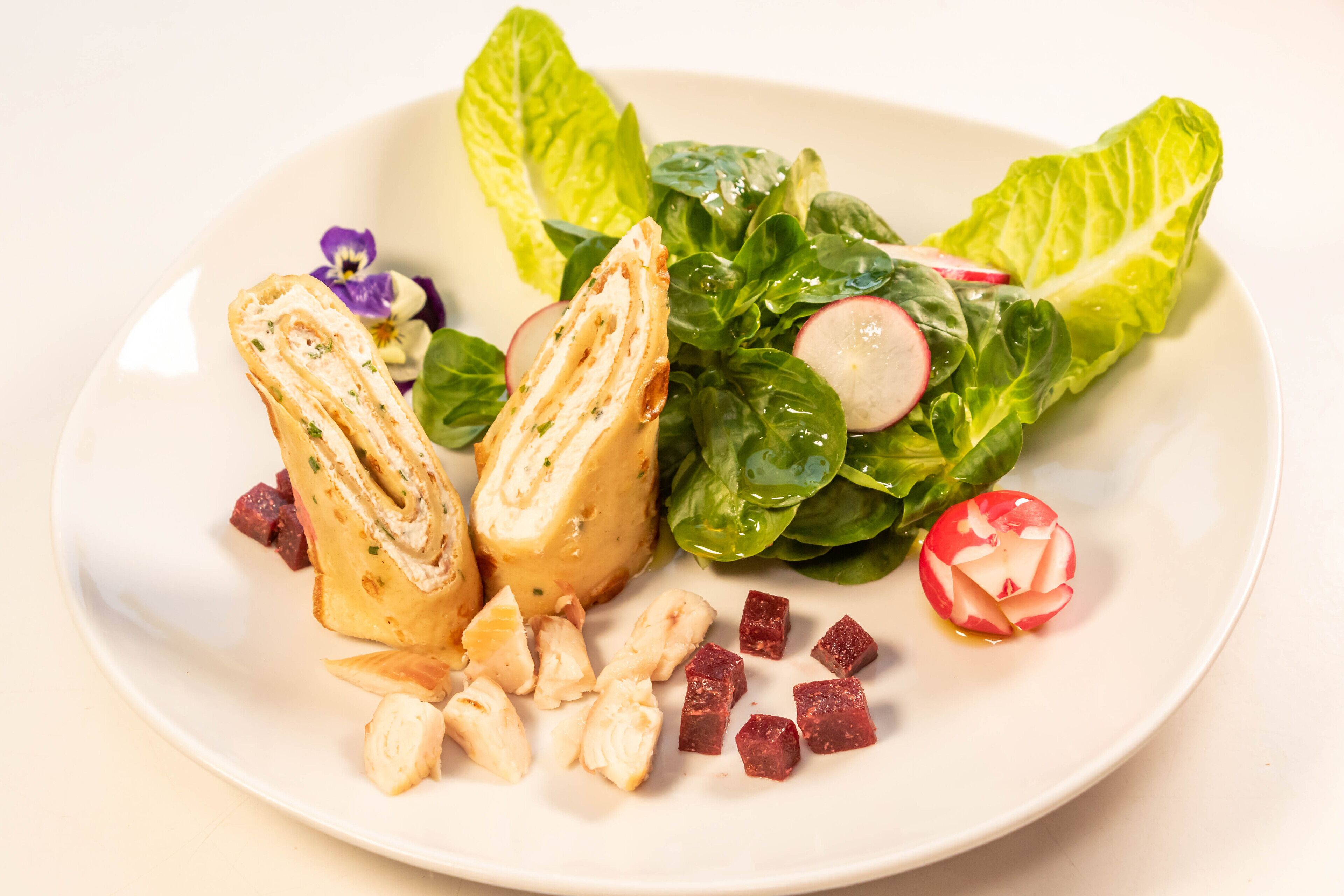 A plate with a sandwich, leafy greens, radishes, and cubes of meat.