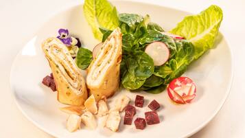 A plate with a sandwich, leafy greens, radishes, and cubes of meat.
