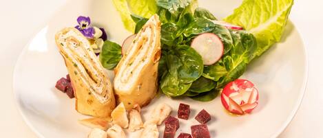 A plate with a sandwich, leafy greens, radishes, and cubes of meat.