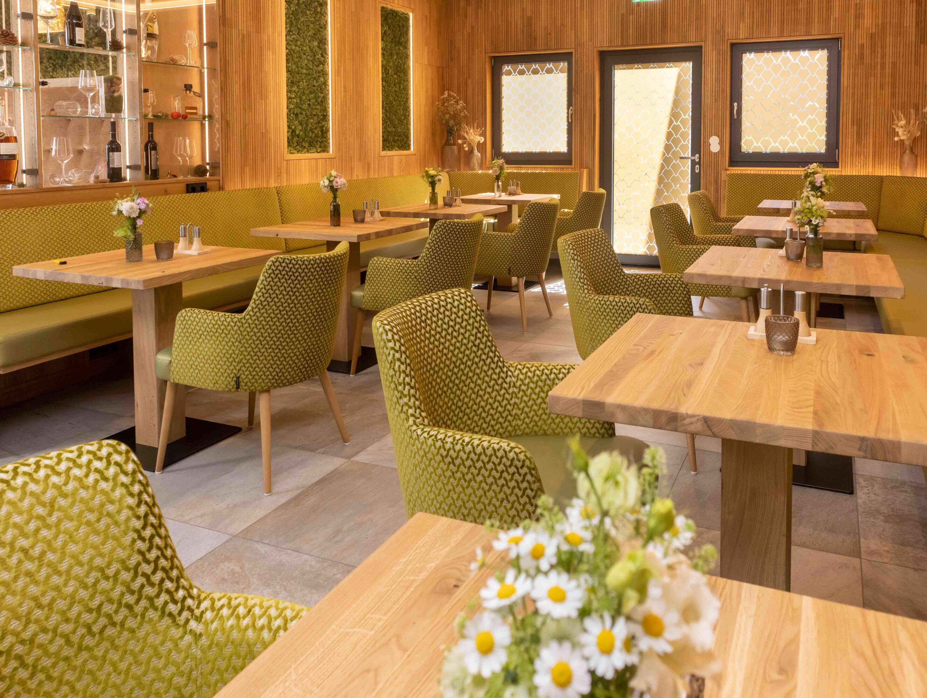Ein Restaurant mit grün gemusterten Möbeln, Holztischen und einer grünen Wand mit vertikalem Garten.
