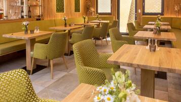 Ein Restaurant mit grün gemusterten Möbeln, Holztischen und einer grünen Wand mit vertikalem Garten.