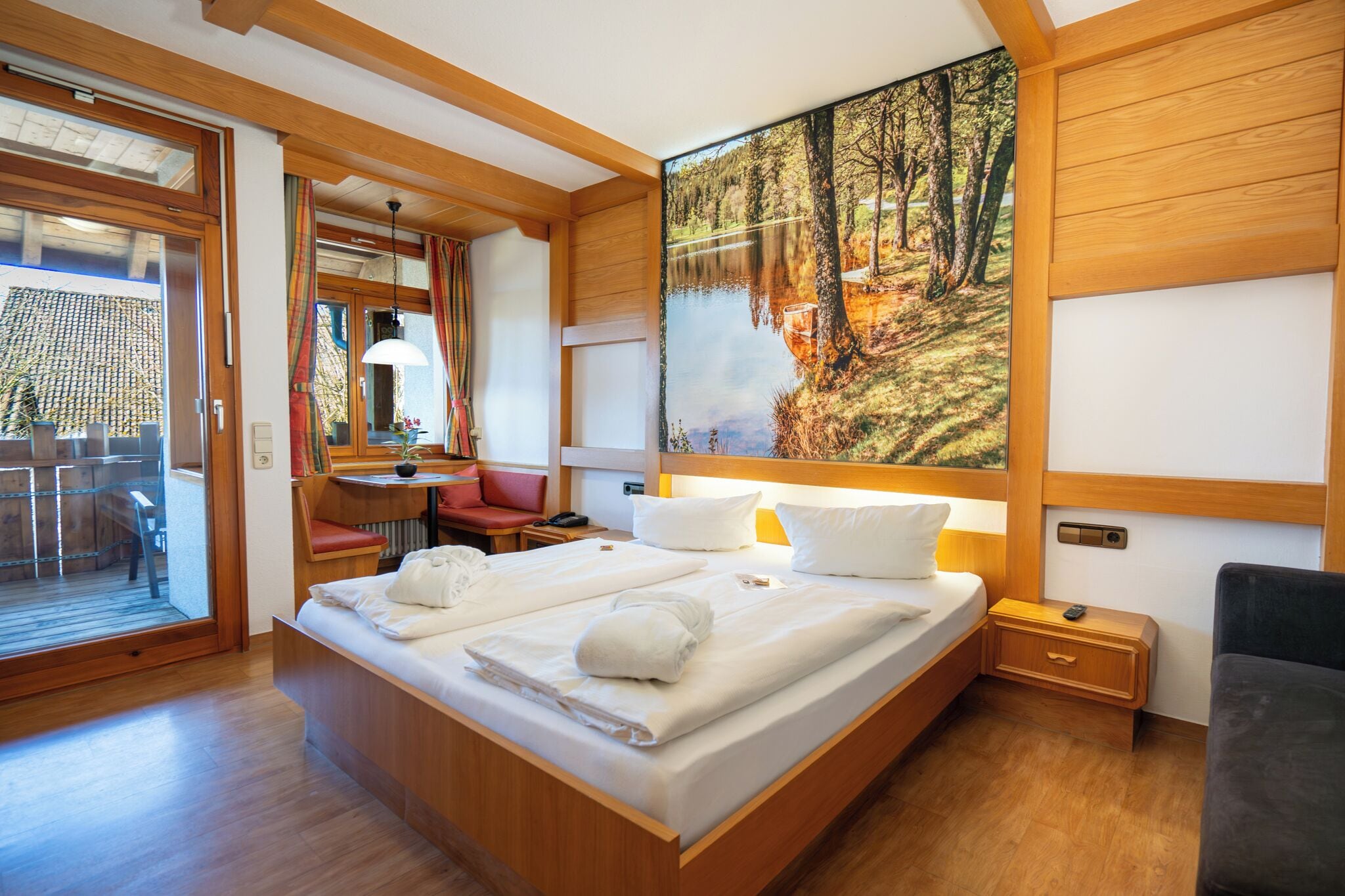 Habitación con una cama grande, un escritorio y una silla. Se ve una ventana con vistas a árboles y un lago.