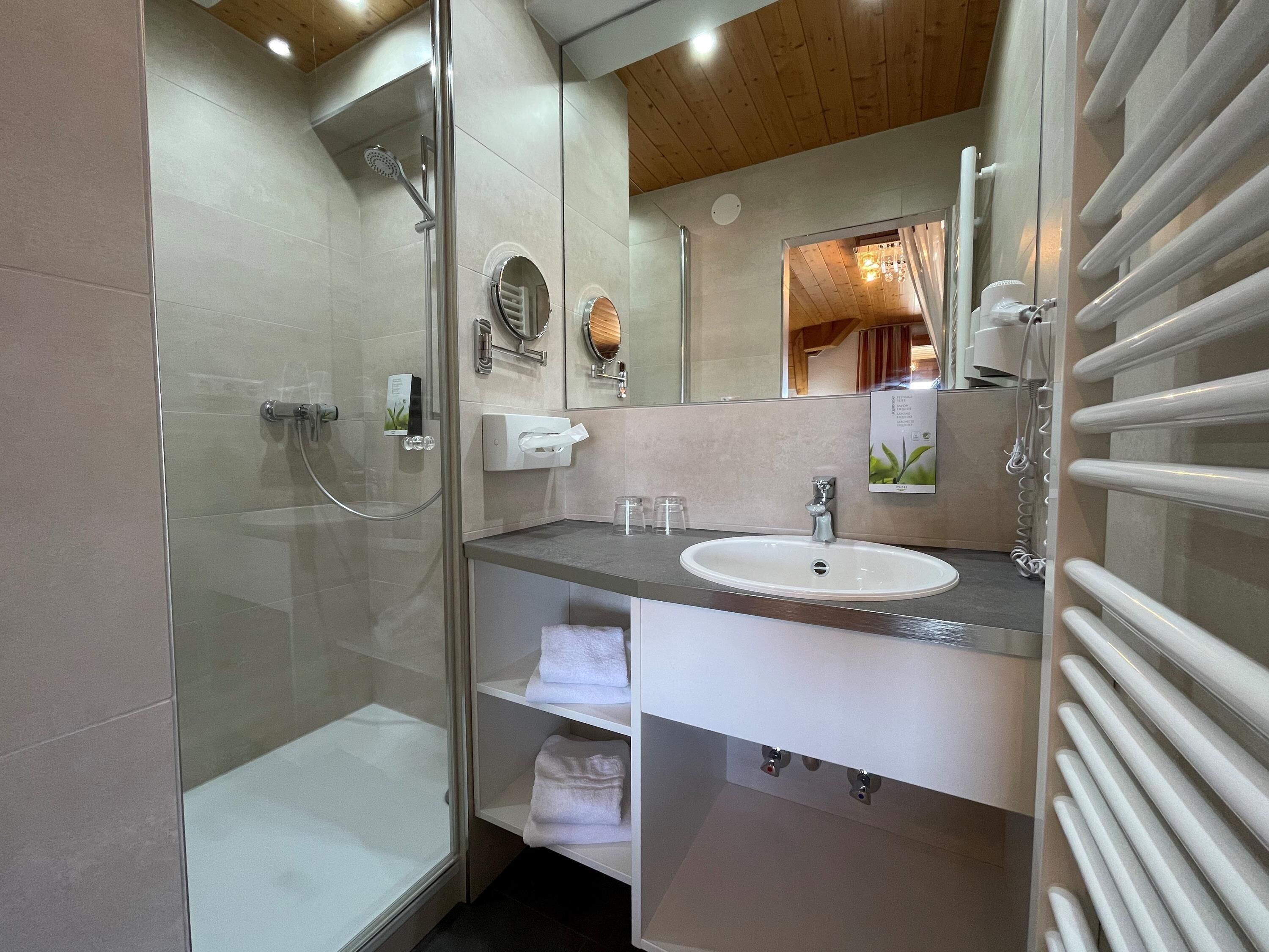 A modern bathroom with a glass-enclosed shower, a white sink, and a towel rack.