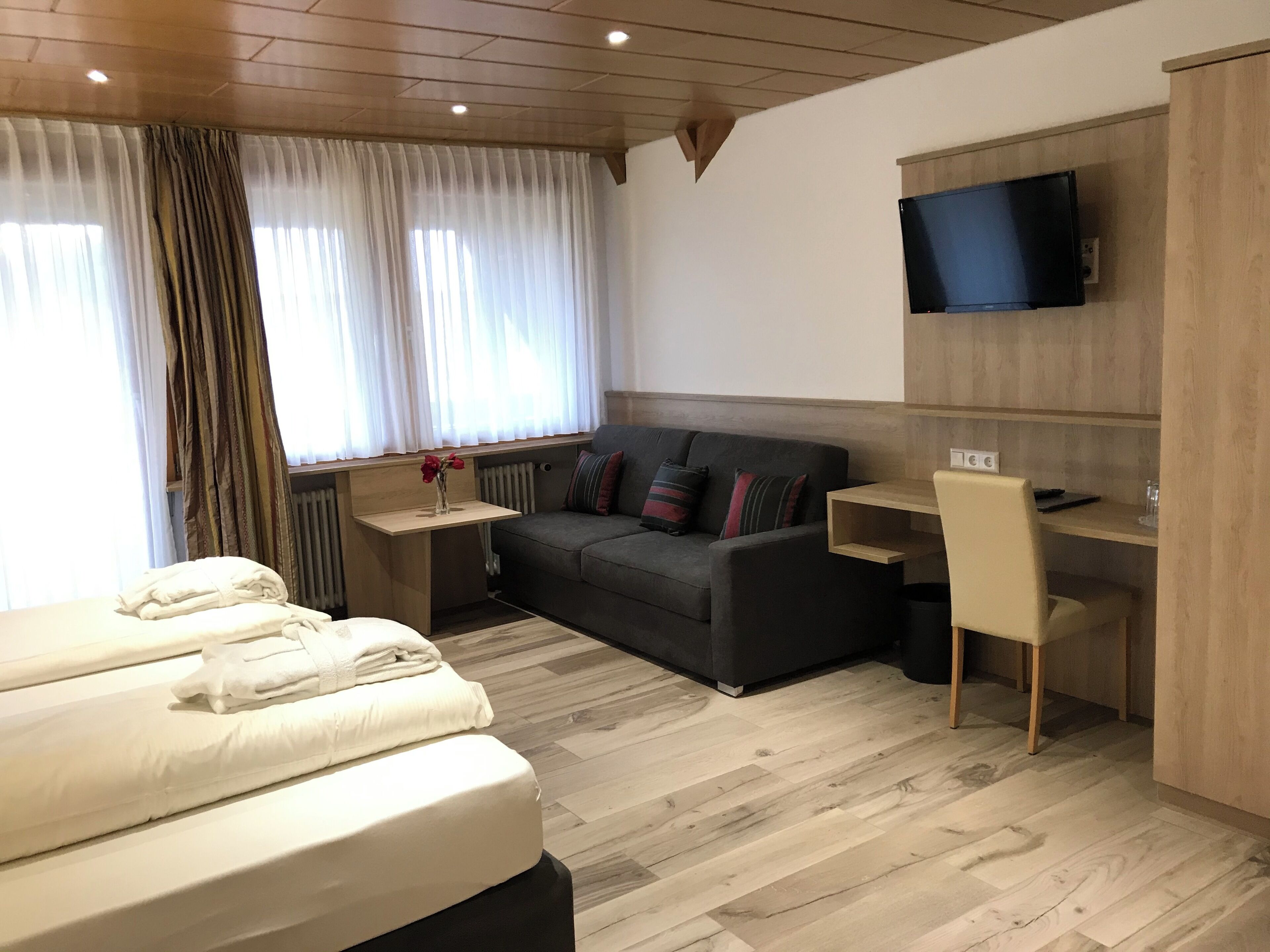 Una habitación de hotel moderna con cama, sofá, escritorio y televisión montada en la pared.