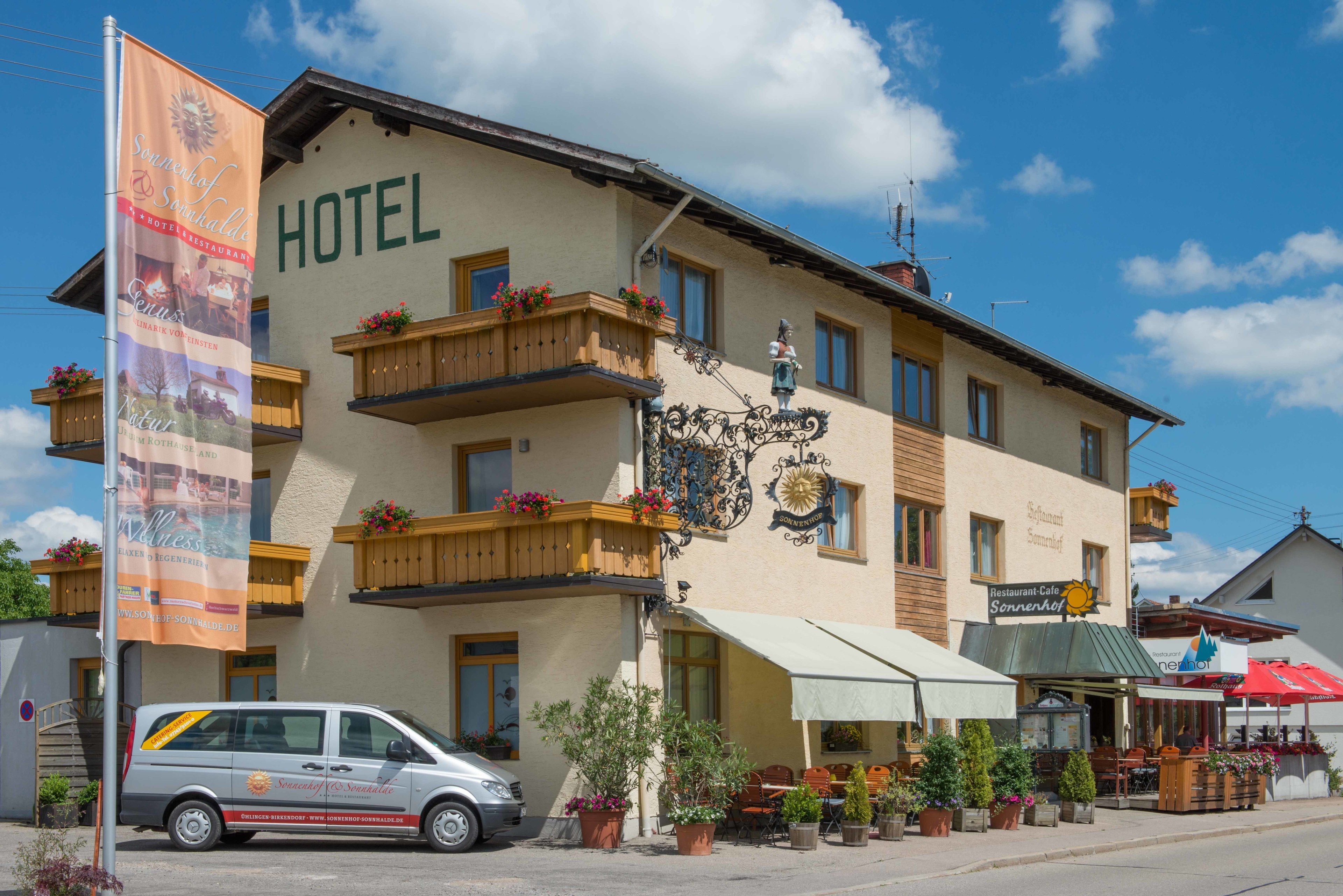 Un hotel con un letrero que dice "HOTEL" y un cartel publicitario para un restaurante. Se ven plantas en macetas y mesas al aire libre.