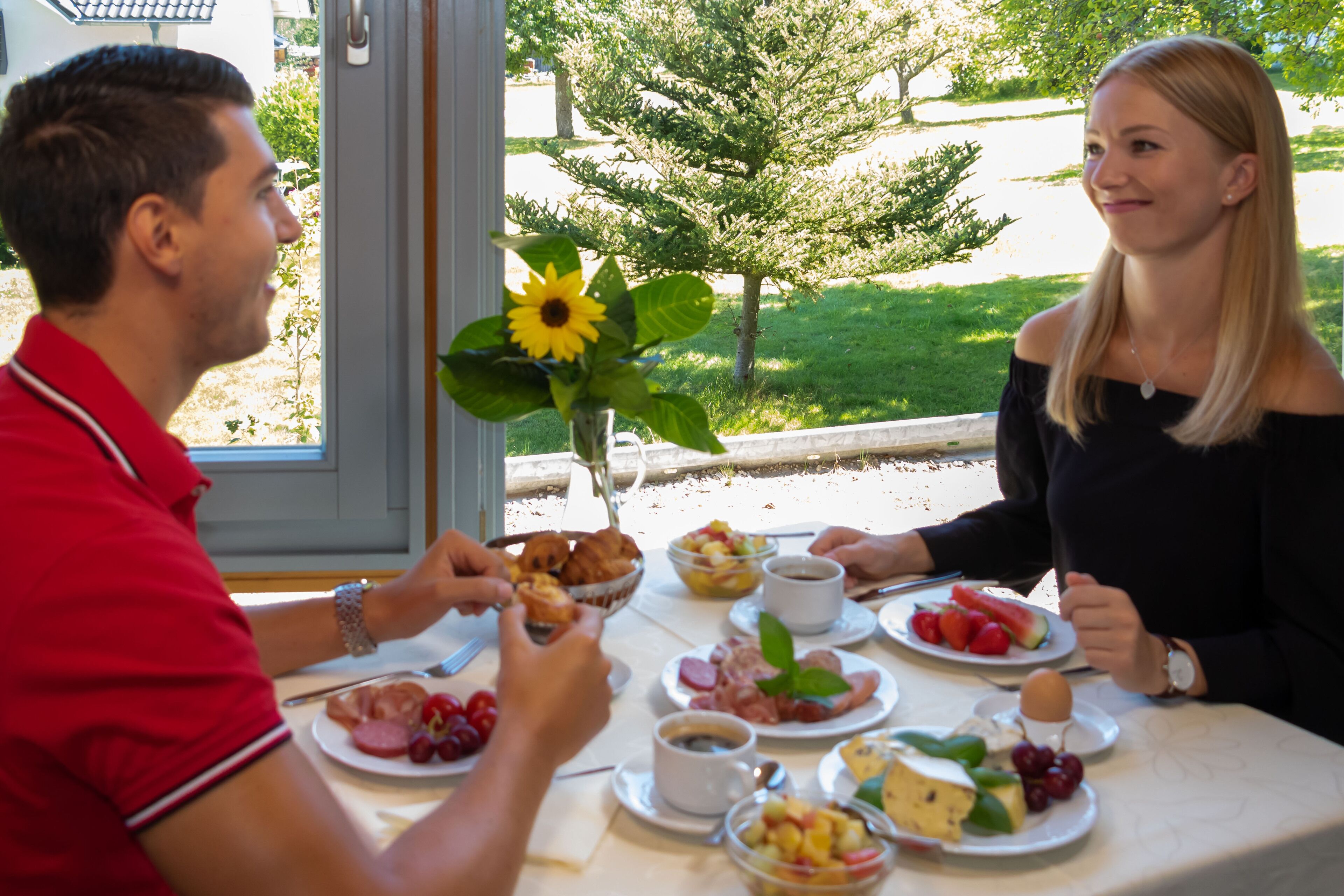 A dining table with breakfast items and a vase of sunflowers.