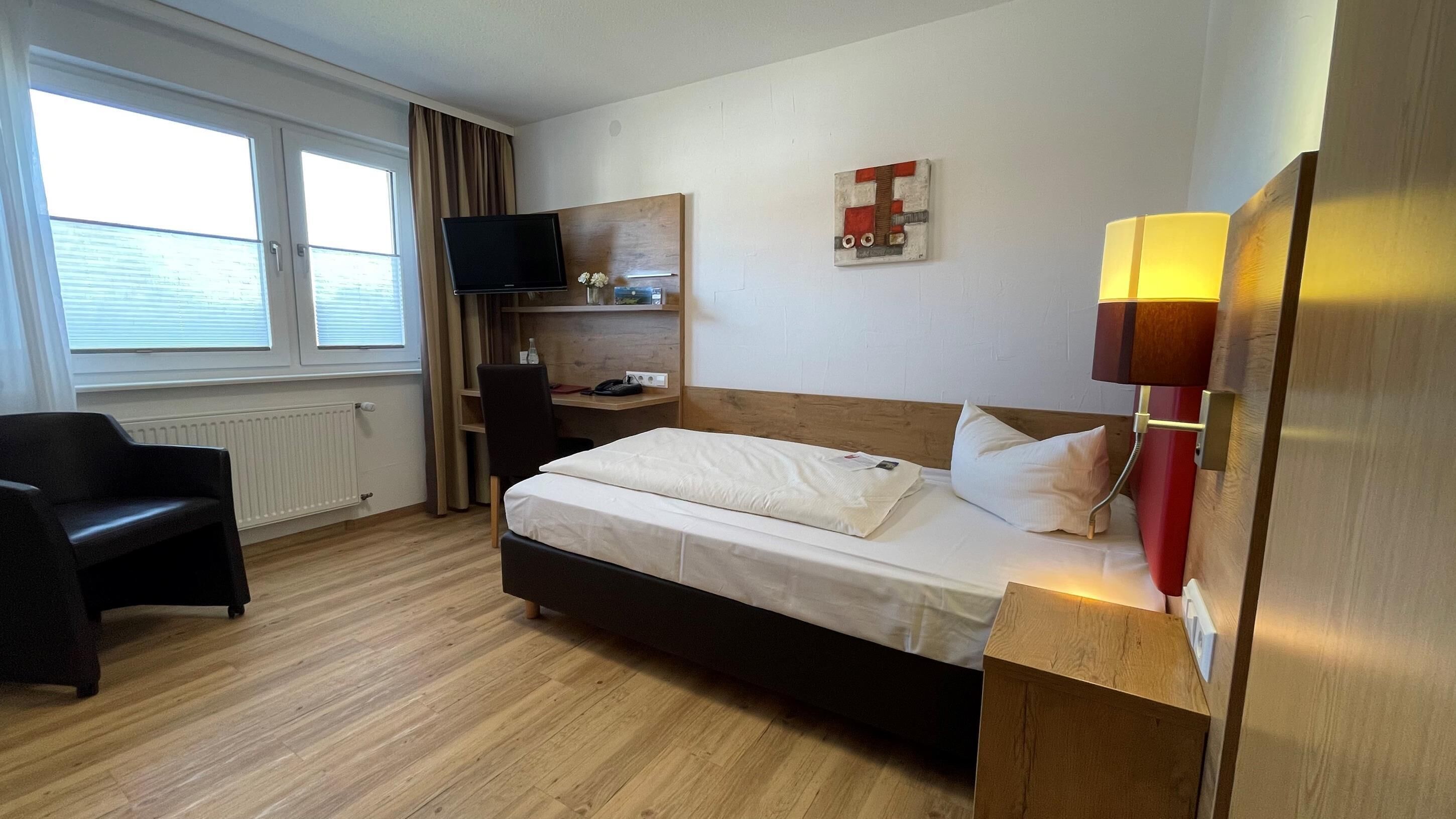 Habitació d'hotel amb llit, escriptori, cadira, televisió i finestra amb cortines.
