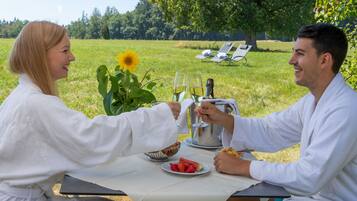 A couple dining outdoors with a table set for two, a bowl of strawberries, a plate of watermelon, and a sunflower.
