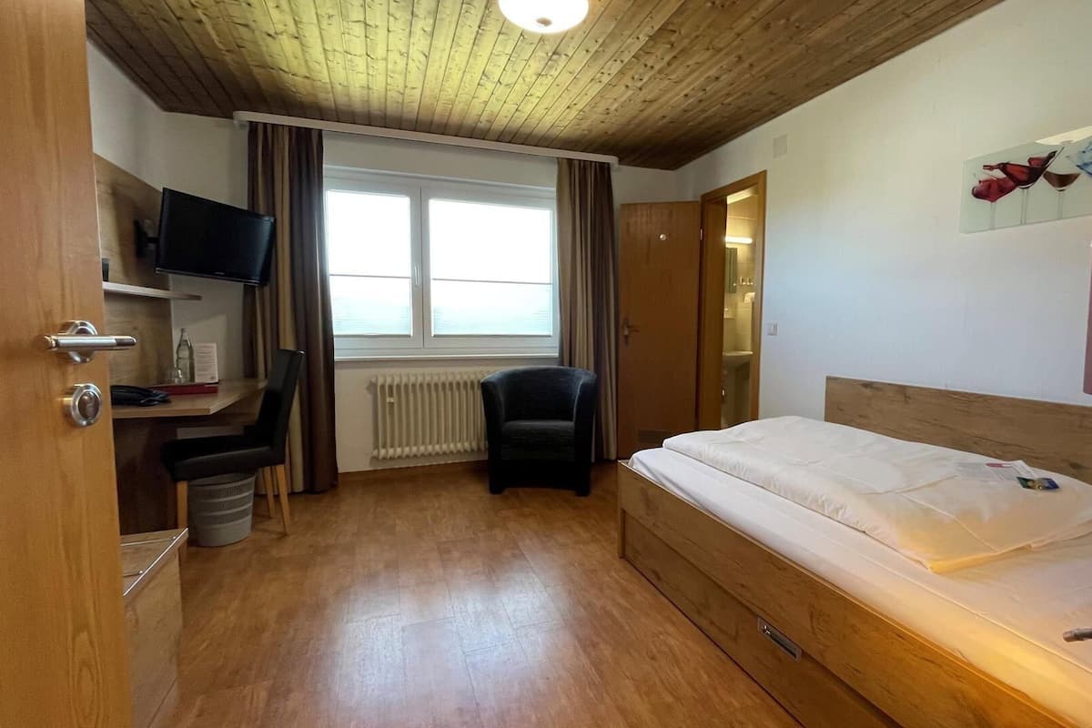 Ein Hotelzimmer mit Holzboden, einem Bett, einem Schreibtisch mit Stuhl, einem Fernseher und einem Fenster mit Vorhängen.