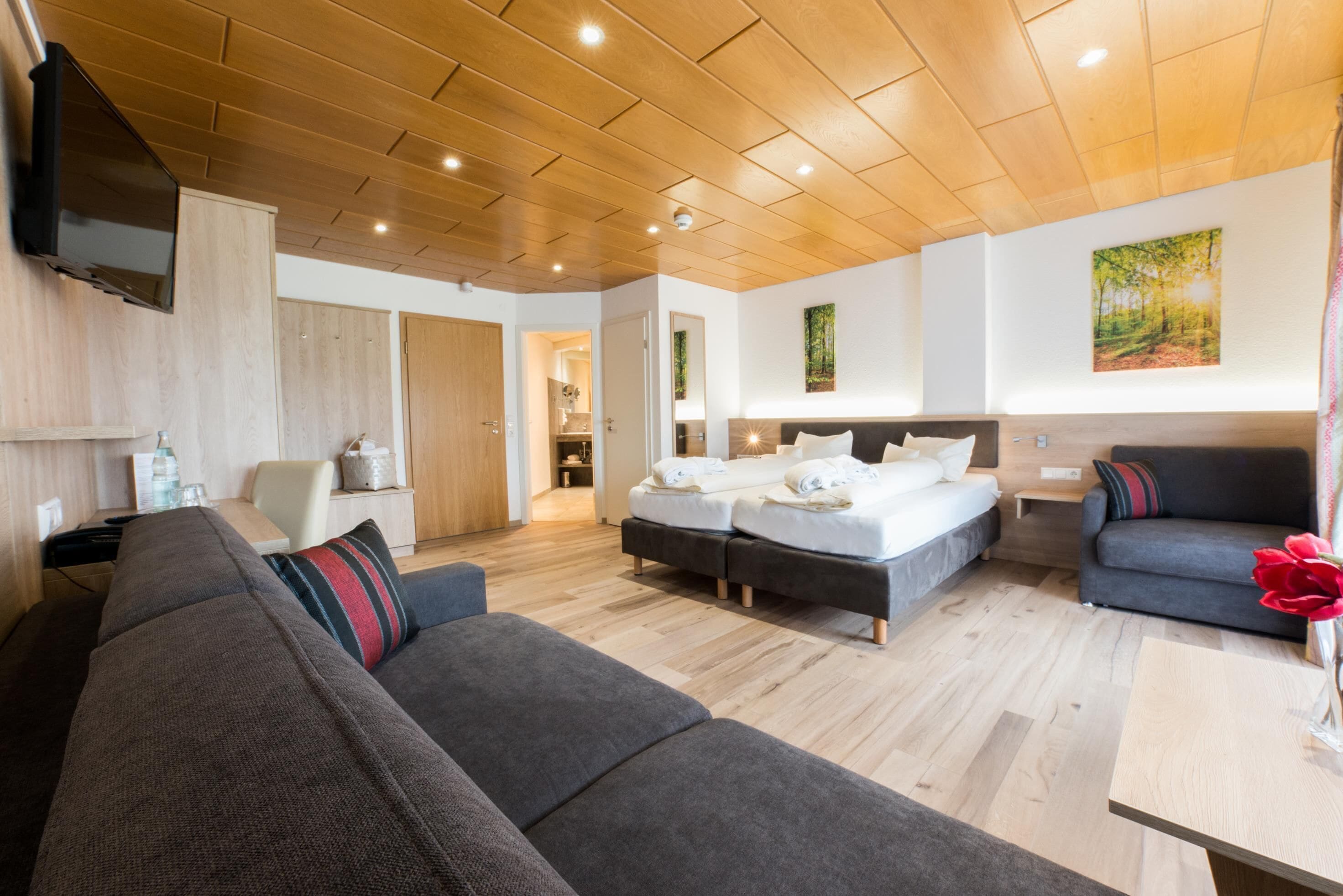 A modern hotel room with a wooden ceiling, a large bed, a sofa, and a dining table.