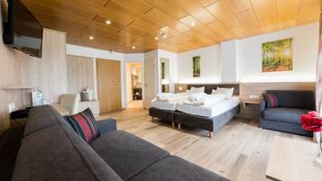 A modern hotel room with a wooden ceiling, a large bed, a sofa, and a dining table.