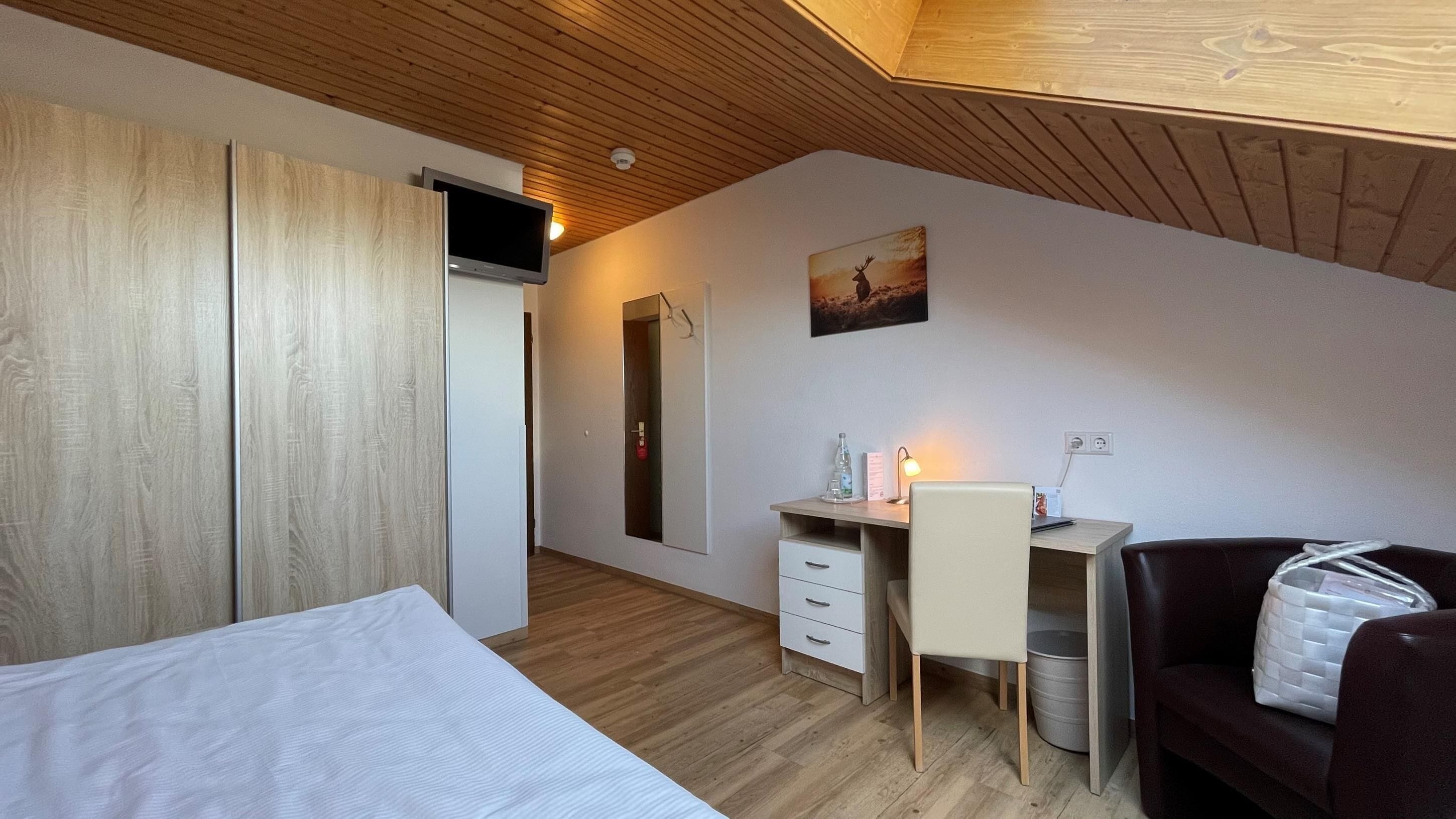 Une chambre d’hôtel moderne avec un plafond en bois, un lit, un bureau avec une chaise, un miroir et un tableau accroché au mur.