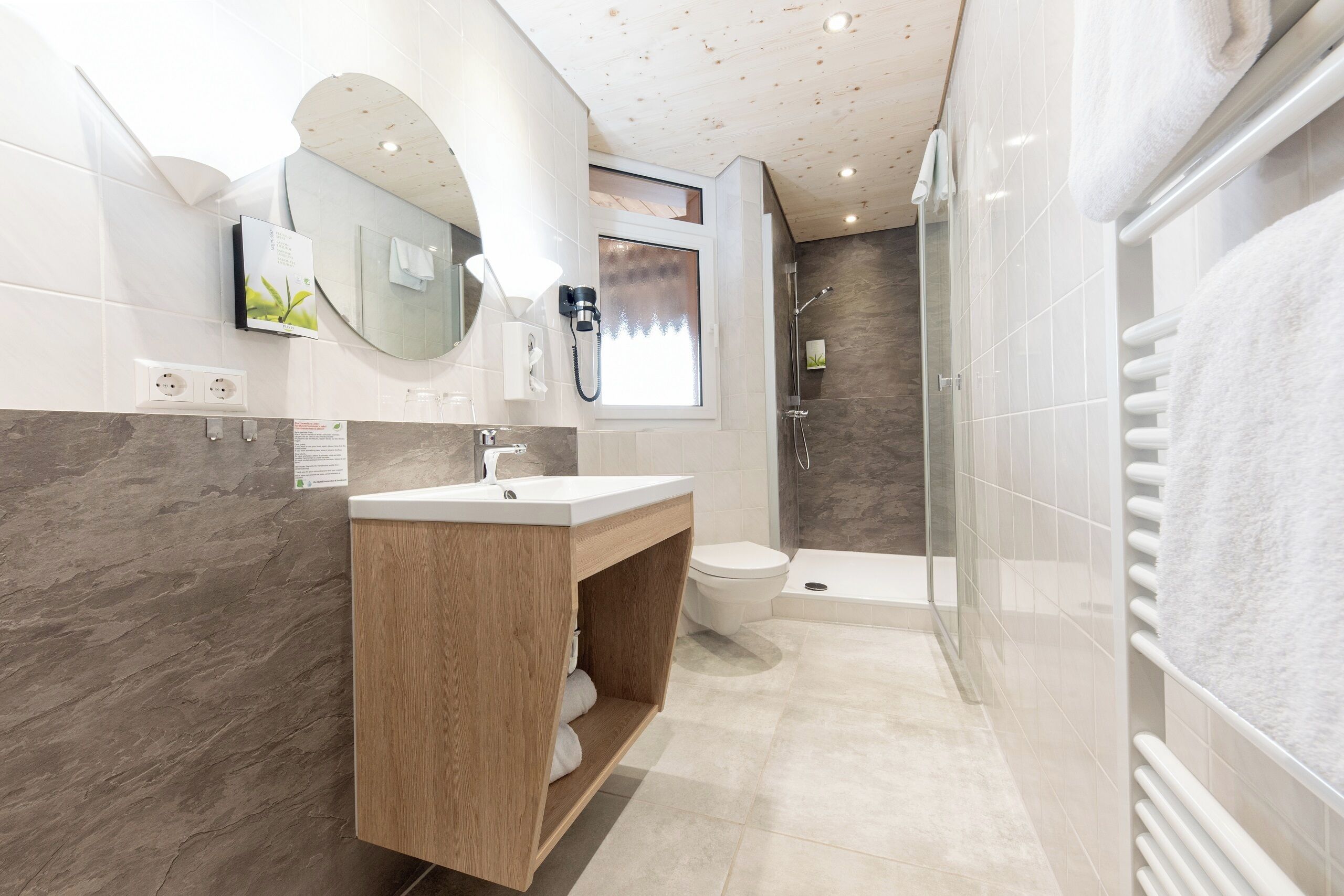 Un baño moderno con tocador de madera, cabina de ducha de vidrio y piso de baldosas blancas.