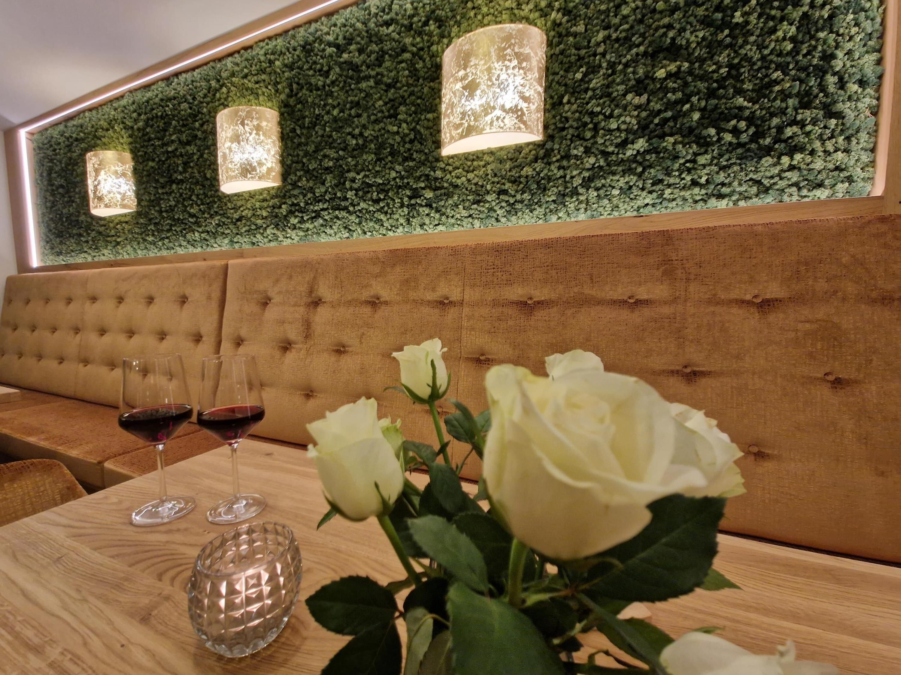 Una mesa de madera con dos copas de vino y un florero de vidrio con una rosa blanca.