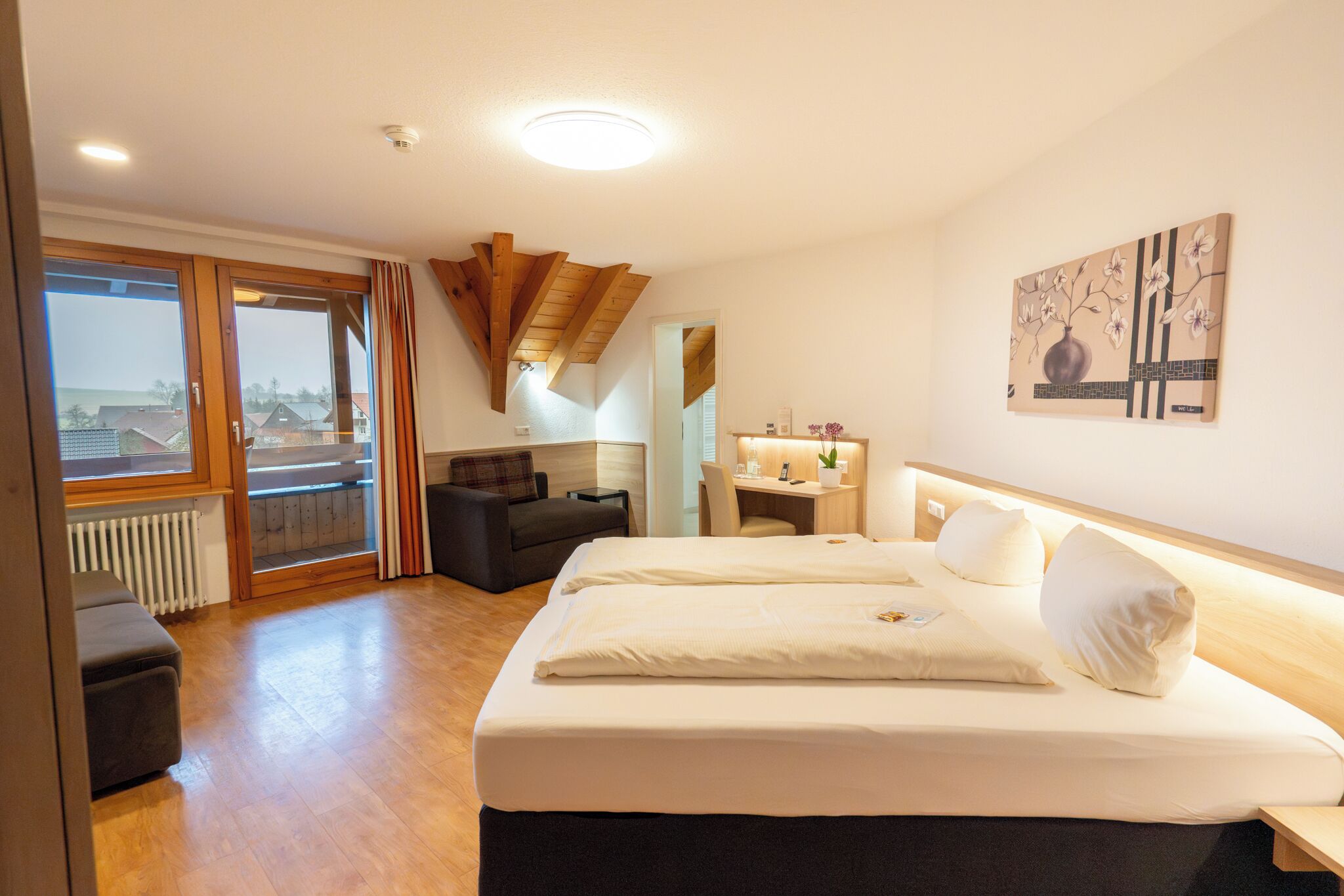 A hotel room with a large bed, a desk, a chair, a sofa, and a view of the outside.