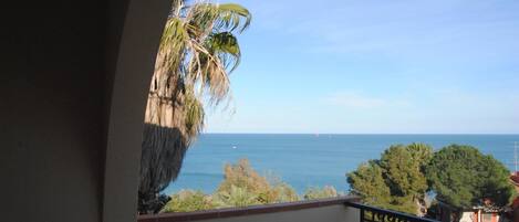 A balcony with a view of the sea and palm trees.