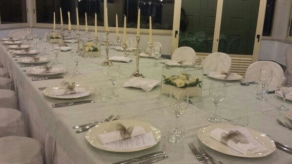 A long dining table set with white tablecloths, candles, and glassware, likely in a formal dining area.