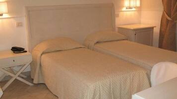 A hotel room with two single beds, a small desk with a phone, and bedside lamps.